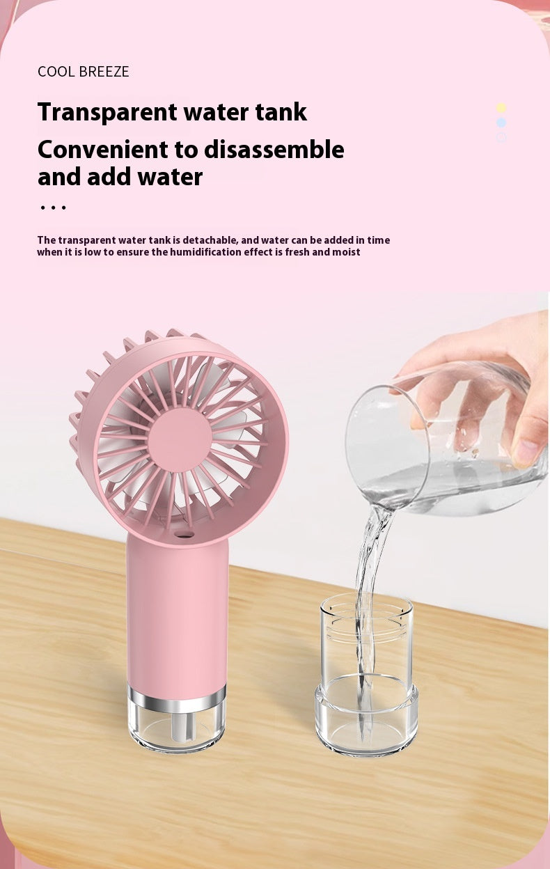 Pouring water into the refillable mist tank of a pink handheld spray fan on a wooden table